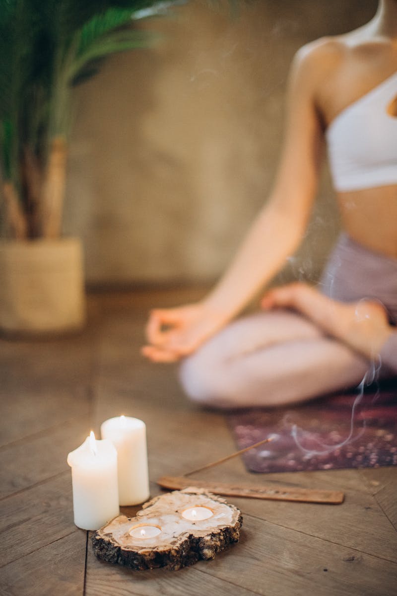 Person meditating on a yoga mat with candles and incense burning in the foreground